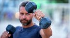 Muscular man performing a dumbbell only training program outdoors Muscular man performing a dumbbell only training program outdoors