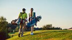 Golfing couple walking the course wearing golf bags Golfing couple walking the course wearing golf bags