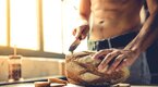 Muscular man cutting a loaf of fresh baked bread in his kitchen with a bread knife for carb loading diet Muscular man cutting a loaf of fresh baked bread in his kitchen with a bread knife for carb loading diet