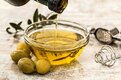 olive oil pouring into a glass dish, with some green olives