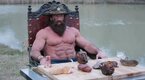 The Liver King sitting at a table with raw meat displayed while next to a river
