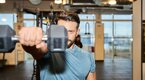 Young physically fit man performing dumbbell front raises to working out his delt muscles